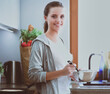 © lenets_tan - Young woman prepares pancakes in the kitchen while standing near the table. Woman in the kitchen. Cooking at kitchen.
