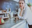 © lenets_tan - Portrait of young woman standing against kitchen background.