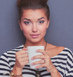 © lenets_tan - Young woman standing with cup, isolated on gray background. Young woman