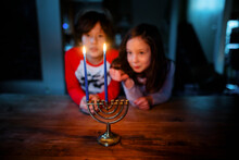 Two Siblings Sit At Table Together Staring At Lit Candles On Menorah