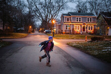 A Boy In Winter Clothes Plays On Lamplit Street At Dusk