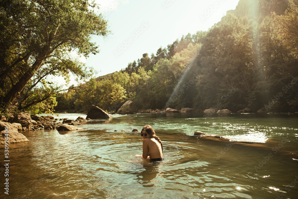 Naked girl bathing in a river surrounded by trees during sunset Stock