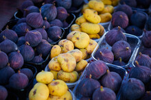Fig Fruits Of Different Varieties On The Counter Of The Farmers Market In The Evening Sunlight. Contrasting Yellow And Purple Fruits Arranged In Rows. Healthy Food Concept