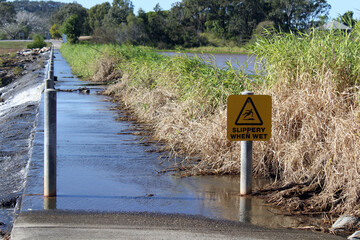 Causeway over a lake with a slippery when wet sign