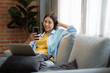 © ijeab - Young asian woman smiling and using smartphone on couch at home.