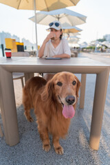 Poster - Woman drinking coffee with her golden retriever in outdoor restaurant