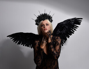 portrait of beautiful  model  wearing black gothic dress with headdress  and feathered angel wings.  isolated on studio background.