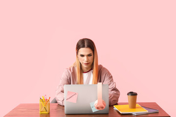 transgender programmer with laptop at table on pink background