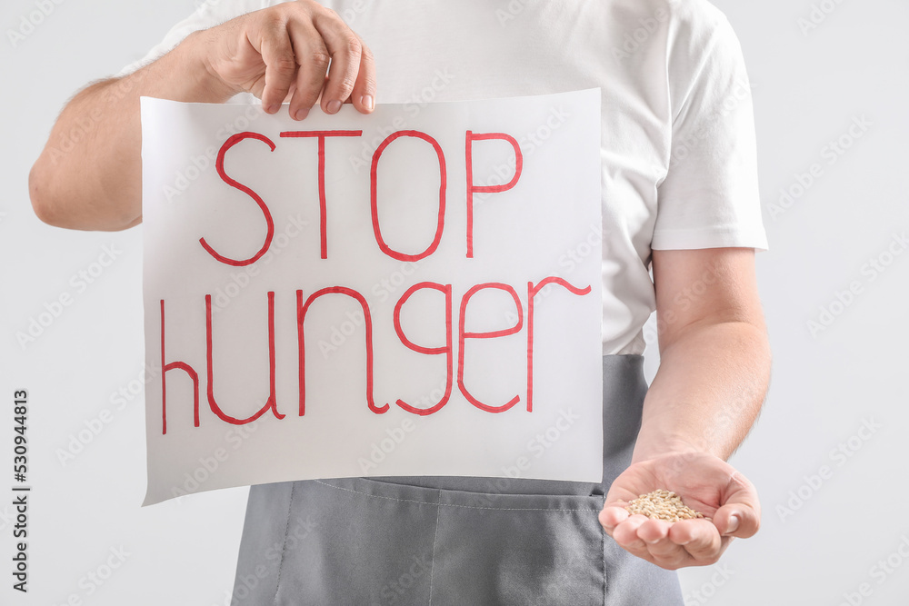 Man holding paper sheet with text STOP HUNGER and wheat grains on light background