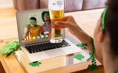 Canvas Print - African american woman holding a beer glass having a video call on laptop at home