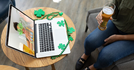 Canvas Print - Mixed race woman holding beer at bar making st patrick's day video call to friend on laptop screen