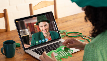 Poster - Caucasian woman holding shamrock glasses while having a video call on laptop at home