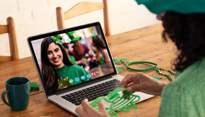 Poster - Caucasian woman holding shamrock glasses while having a video call on laptop at home