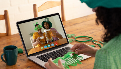 Poster - Mixed race woman making st patrick's day video call to male friends holding beers on laptop at home