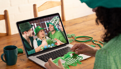 Poster - Mixed race woman making st patrick's day video call to friends in costume on laptop at home