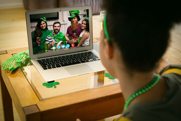 Wall Mural - Mixed race woman making st patrick's day video call to friends in costume on laptop at home