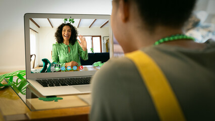 Sticker - Mixed race woman making st patrick's day video call to waving female friend on laptop at home