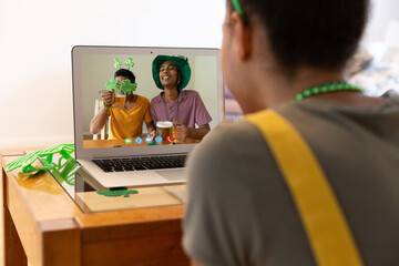 Sticker - Mixed race woman making st patrick's day video call to male friends holding beers on laptop at home