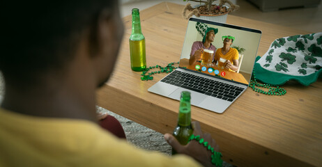 Poster - African american man holding beer having st patrick's day video call with friends on laptop at home