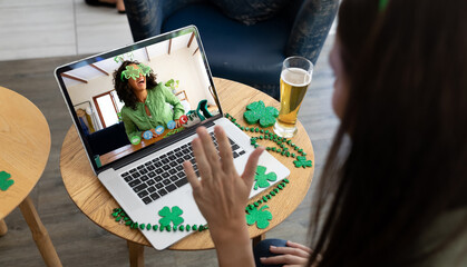 Canvas Print - Caucasian woman at bar making st patrick's day video call waving to friend in costume on laptop