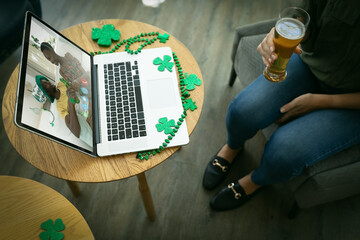 Wall Mural - Mixed race woman holding beer at bar making st patrick's day video call with friends on laptop