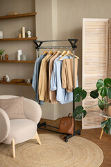 Wall Mural - Trendy capsule wardrobe in beige and light blue on a rail rack against the backdrop of a screen in a modern living room.