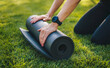 © Strelciuc - Woman hands untwist a black mat for yoga on the green grass in the summer park. Sport and healthy lifestyle concept. Relaxation practicing yoga meditation