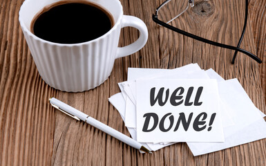 WELL DONE text on sticky with coffee and pen on wooden background