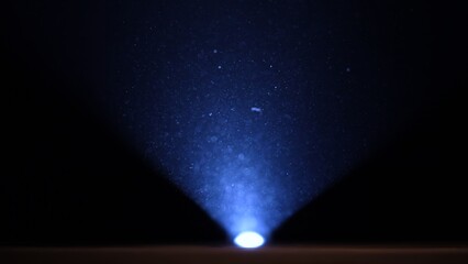 Small particles of dust illuminated by a blue beam of light on a black studio background. Powder or dust floating in a smoky space in the dark. Dust and fog in light of spotlight or flashlight.