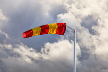 Yellow And Red Striped Windsock Or Wind Cone Against Cloudy And Stormy Sky, Indicating Wind Direction And Force. Copy Space For Your Text.