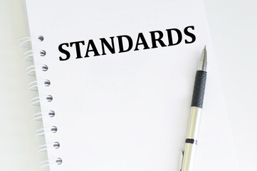 STANDARDS text on notepad on a light desk next to the pen lies