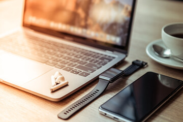 Wall Mural - Close-up of Keyboard laptop computer, wireless earphones focus with smartwatch and smartphone empty screen on wooden background office desk in coffee shop like the background