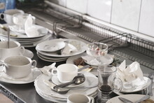 Dirty Plates And Glasses After A Meal In The Kitchen In The Restaurant. Heap Or Pile Of Unclean Glass And Plates Of Breakfast Or Lunch Table.