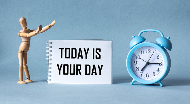 Alarm clock, wooden doll and notebook with the word Today is Your Day on a blue background