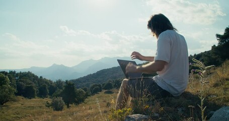 Men sitting on mountain hill with epic landscape using laptop computer outdoors. Male traveler or freelancer working on notebook. Guy typing on keyboard. Online cyberspace and technology