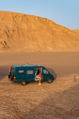 Wall Mural - Woman standing next to her campervan in the desert at sunset