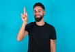 © Jihan - young bearded hispanic man wearing black T-shirt over blue background pointing up with fingers number ten in Chinese sign language Shi