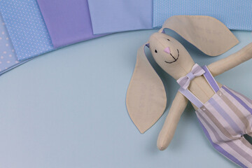 Handmade textile toy for home and interior. Soft toy Rabbit for children. Bunny in a striped suit with a bowtie around his neck. On a blue background