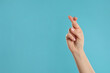 © New Africa - Woman holding fingers crossed on light blue background, closeup with space for text. Good luck superstition