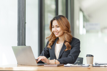 Confident pretty asian business woman working with laptop while doing some paperwork at the office workplace.