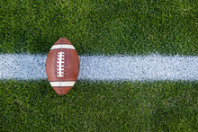 View From Above Of An American Football Sitting On A Grass Football Field On The Yard Line. Generic Sports Image. Lots Of Copy Space
