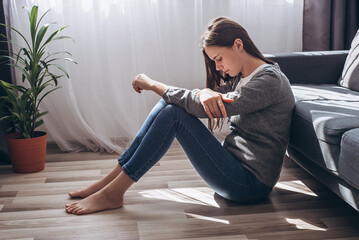 Upset barefoot young woman sitting on floor near couch in living room suffering from bad relationship. Stressed unhappy caucasian female feeling depressed, thinking of personal problems at home