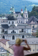 Rear View Of A Woman Taking A Photograph Of Cathedral And Cityscape, Salzburg, Austria