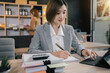 © NINENII - Business woman sitting on desk using laptop. Portrait of busy secretary typing in working environment. Happy young businesswoman in casual working on computer in office.