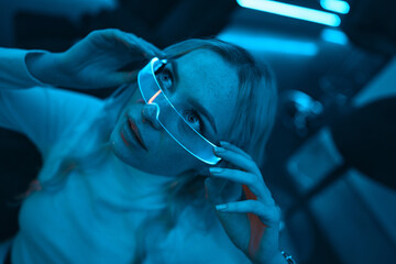 Neon blue light falls on a young woman wearing futuristic glass glasses.