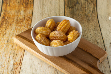 Wall Mural - brazilian mini churros, a traditional snack for party with sugar and cinnamon powder in a white container and wooden background