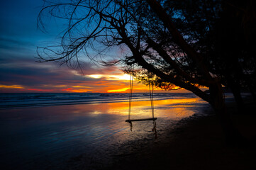 Wall Mural - silhouette swing at seaside beach , evening time twilight sky over island in ocean background