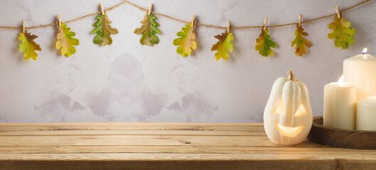 Wall Mural - Wooden table with jack o lantern pumpkin and candles over autumn leaves garland background. Halloween holiday mock up for design and product display