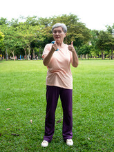Portrait Of Mature Asian Woman 60s Wearing Sports Clothing Doing Arm Work Out And Lifting Dumbbell Exercise With Relaxation For Healthy In Park Outdoor.