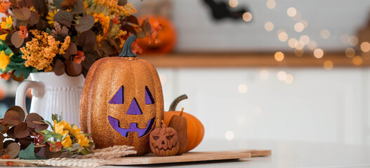 A vase of flowers,a jack pumpkin and candles on a tray. In the background - the interior of a white kitchen in Scandi style. The concept of home and comfort. Autumn decor for the Halloween holiday.